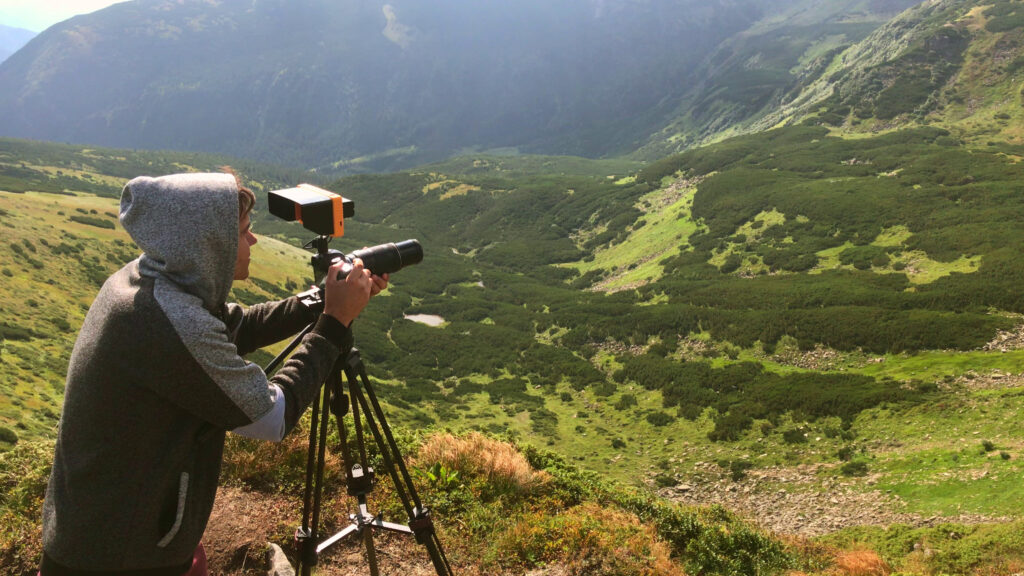 Man filming with a camera and tripod in the mountains
