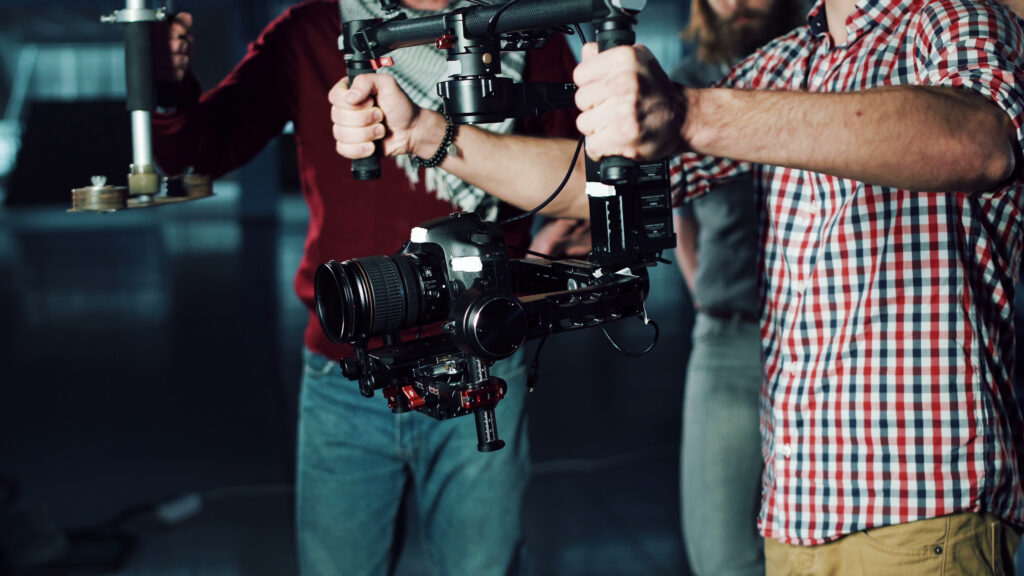 Still Image of Man Testing Handheld Camera Gyro Stabilizing Gimbal Stretching Arms With Device And Following The Moves Of Stage Director